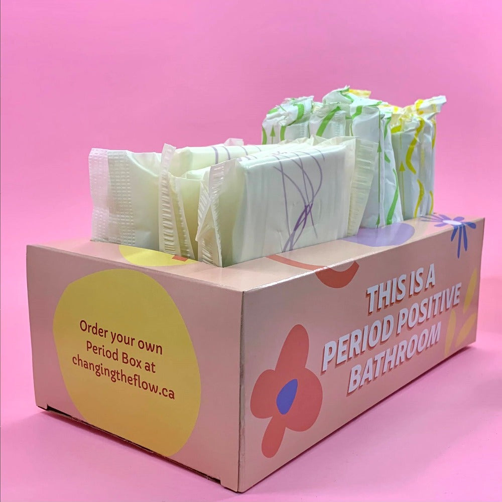 Phot of Your Period Box, with pads and tampons inserted. On teh front of the box it says "This is a period positive bathroom". On the left side it says "Order Your Own Period Box at changingtheflow.ca" in a yellow circle